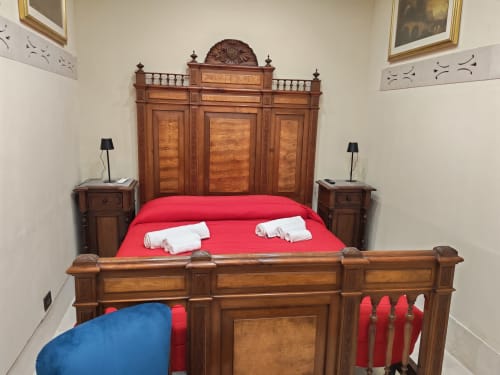 Elegante letto in legno con biancheria rossa e asciugamani bianchi presso Sicily Confort Maison, Linguaglossa, con arredi antichi e
