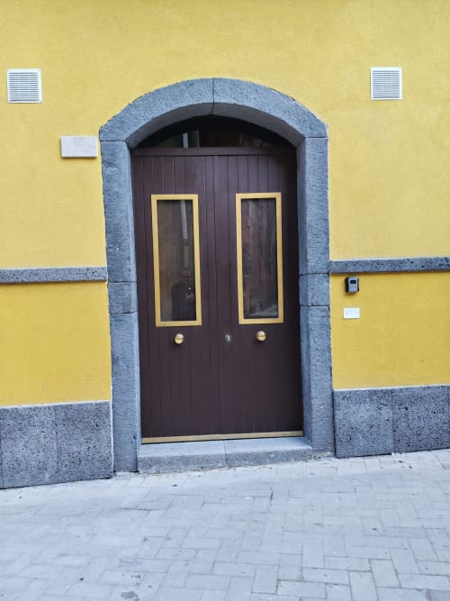 Doppio portone in legno scuro con cornici gialle sulla facciata gialla di Sicily Confort Maison a Linguaglossa