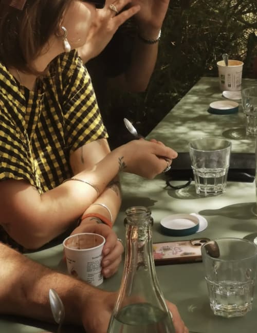 Des clients dînant en terrasse à La Maison d'Ambronay, savourant des boissons et des conversations à la lumière naturelle.