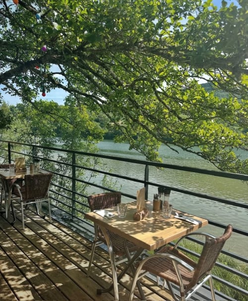 Terrasse riveraine à La Maison d'Ambronay avec chaises en rotin, table en bois et canopée verdoyante surplombant