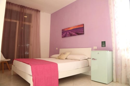 Camera Lavanda presso The Flower Garden B&B a Castellammare di Stabia con pareti rosa, letto bianco, quadri con vista sul paesaggio montano e