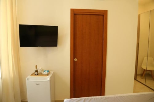 Angolo camera d'hotel con TV a parete, frigorifero, porta in legno e specchio al Flower Garden, Castellammare di Stabia