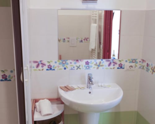 Bagno privato nella camera Girasole del The Flower Garden B&B, con lavabo a piedistallo bianco e decorativo bordo di piastrelle floreali colorate