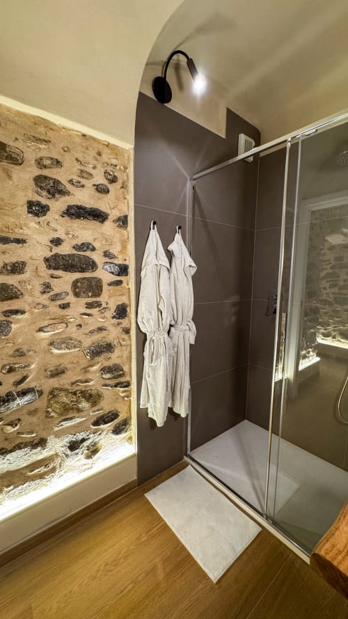 Modern bathroom in Nervia room at Talking Stones B&B, Dolceacqua, featuring stone wall and glass shower enclosure