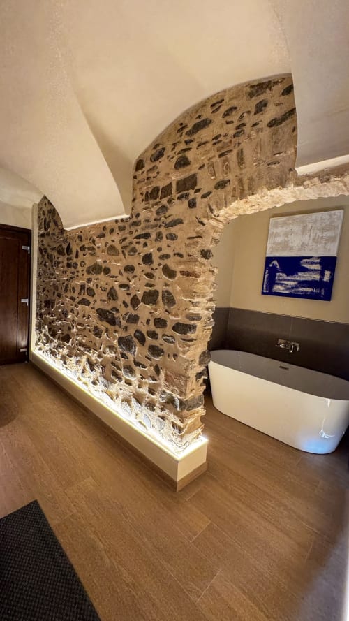 Modern spa bathtub in Nervia N°22 at Talking Stones Group, Dolceacqua, with exposed stone wall and ambient lighting