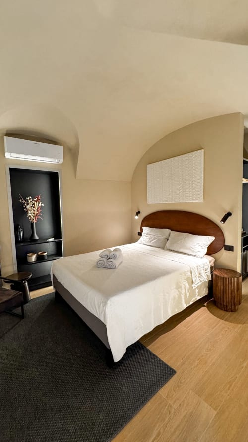 Modern bedroom at Talking Stones in Dolceacqua with wooden headboard, white bedding, and curved archway design