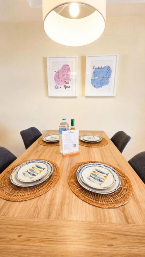 Comedor moderno en apartamento Aloha Calpe con mesa de madera, salvamanteles de mimbre y mapa de la ciudad enmarcado en la pared.