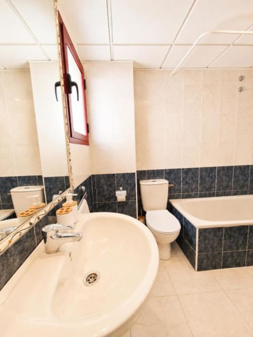 Baño moderno en Aloha Apartment, Calpe con lavabo redondo, bañera, inodoro, detalles de azulejos oscuros y espejo.