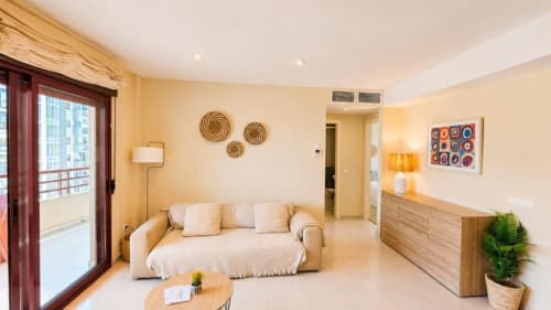 Luminosa sala de estar en Aloha Apartment, Calpe con sofá beige, muebles de madera, decoración costera y acceso a balcón con vista al mar