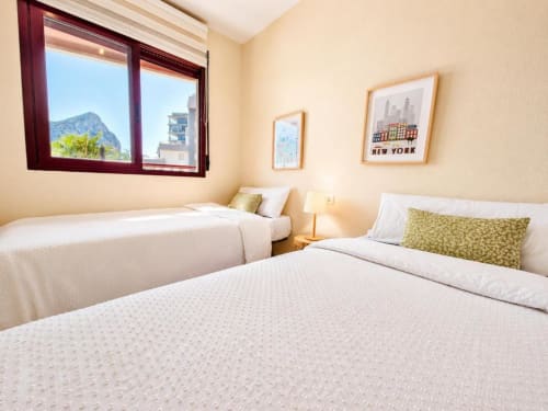 Luminoso dormitorio de apartamento Aloha en Calpe con vistas al mar, dos camas, detalles en oliva y arte de NYC enmarcado
