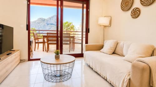 Apartamento Aloha en Calpe con sofá beis, vistas a la montaña desde las puertas de la terraza, mesa de café moderna y arte mural