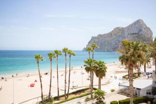 Apartamento Aloha Calpe con vistas al mar, palmeras, playa de arena blanca, aguas turquesas y la icónica roca del Peñón de Ifach