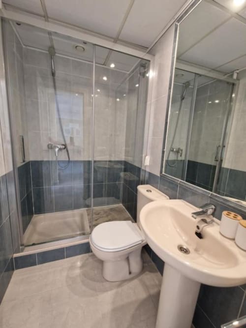 Baño moderno en Aloha Apartment, Calpe con ducha de cristal, lavabo blanco, inodoro y detalles en azulejos oscuros