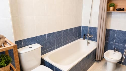 Baño moderno en Apartamento Aloha, Calpe con bañera blanca, WC, bidé, azulejos azules y beige, y área de ducha