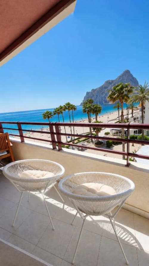 Balcón con sillas blancas con vistas a la playa de Calpe, palmeras y el Peñón de Ifach, Apartamento Aloha