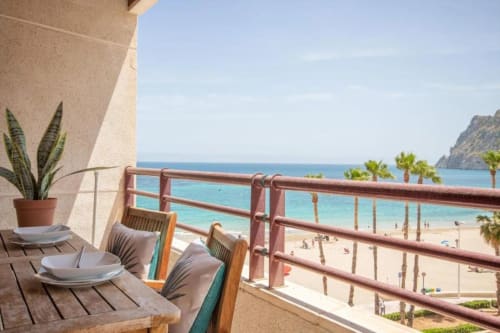 Terraza del apartamento Aloha Calpe con vistas al mar, mesa de comedor, planta decorativa y playa arenosa con palmeras