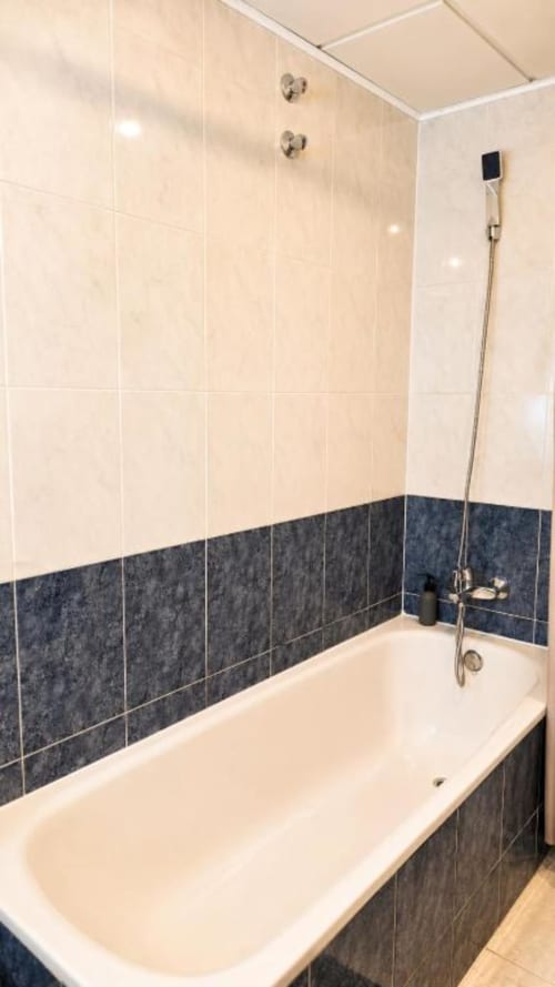 Baño moderno con bañera blanca, doble ducha y detalles en azul oscuro en apartamento Aloha Calpe