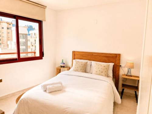 Dormitorio luminoso en dúplex Aloha Calpe, con cama de madera, ropa de cama blanca, vistas al mar y mobiliario moderno