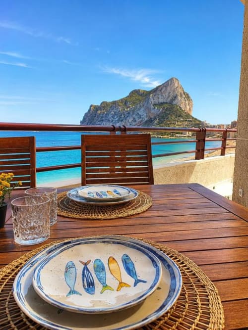 Terraza junto al mar en Aloha Calpe con platos decorados de peces, comedor de madera y vistas al Peñón de Ifach, Calpe España