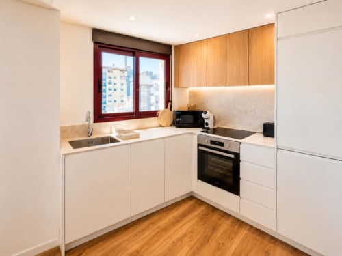 Cocina moderna del apartamento dúplex Aloha Calpe, Calpe con muebles blancos, detalles de madera, horno de acero inoxidable y vistas a la ciudad