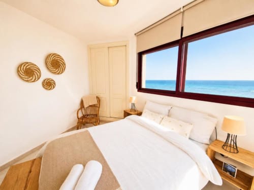 Luminoso dormitorio frente al mar en Aloha Calpe con vistas al océano, cama blanca, decoración de ratán y vista al mar desde amplias ventanas