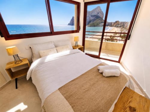 Dormitorio luminoso con vistas al mar en Aloha Calpe. Cama blanca, mesillas de madera, balcón moderno con vistas al Mediterráneo