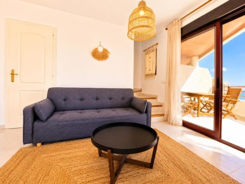 Elegante sala de estar en dúplex Aloha Calpe con sofá gris, mesa de centro negra y vistas al mar desde las puertas de la terraza