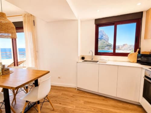 Moderna cocina y comedor en dúplex de Calpe con vistas al mar y montañas al fondo a través de las ventanas