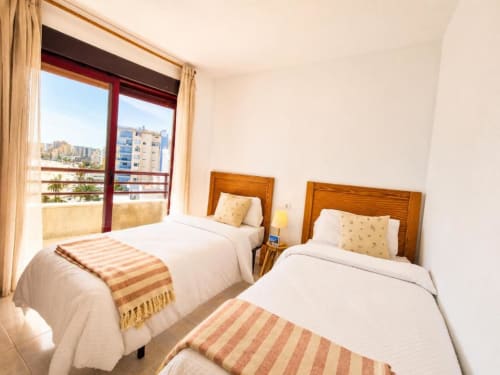 Camas gemelas con cabeceros de madera en luminoso dúplex Aloha Calpe, con balcón con vistas al mar y horizonte de la ciudad