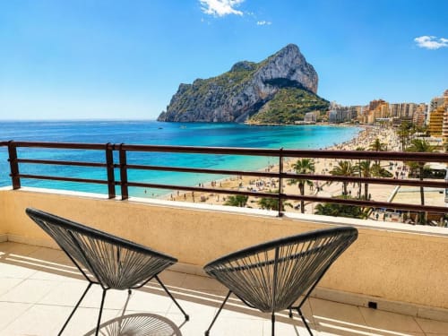 Balcón con tumbonas con vistas a las aguas turquesas del Mediterráneo, playa de Calpe y emblemática formación rocosa en Aloha Calpe