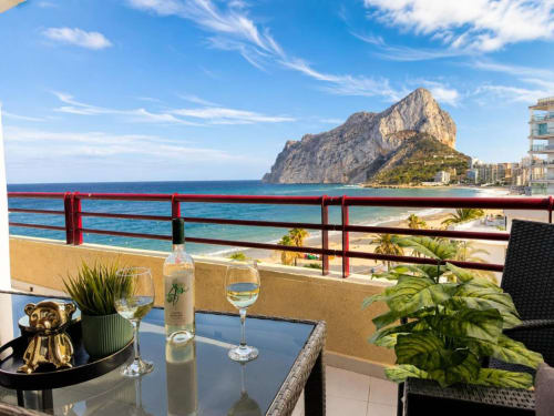 Vistas desde el balcón Aloha Calpe con copas de vino frente al Peñón de Ifach y la playa mediterránea