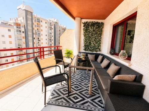 Terraza moderna del apartamento Aloha Calpe en España con muebles de ratán negro, alfombra geométrica y vistas residenciales