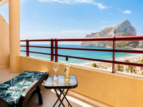 Balcón de apartamento dúplex en Aloha Calpe con vistas al mar, tumbona, copas de vino y formación rocosa del Peñyal d'Ifach