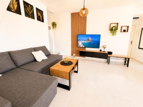 Salón moderno en dúplex Aloha Calpe con sofá gris, mesa de café de madera, TV de pantalla plana y vistas al mar