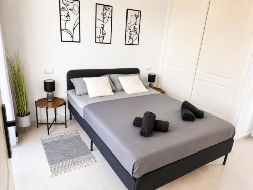 Moderno dormitorio en Apartamento Dúplex Aloha Calpe II, Calpe con cama gris, cabecero negro, decoración neutral y obra de arte con vistas al mar.