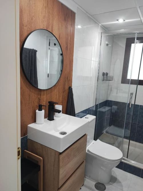 Baño moderno en Apartamento Dúplex Aloha Calpe II con mueble de madera, espejo circular, ducha de cristal y acabados en azulejos blancos