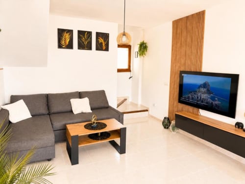 Moderno salón en Apartamento Duplex II de Aloha Calpe con sofá gris, mesa de café de madera, TV plana y vistas al mar