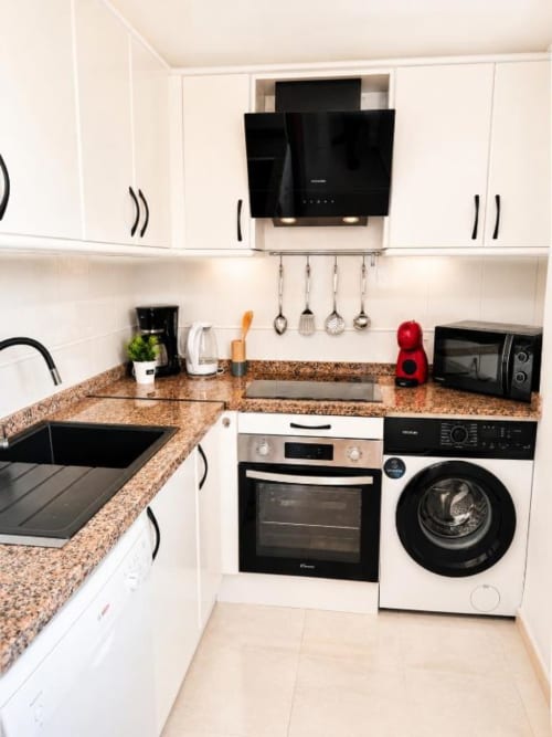 Cocina moderna en duplex Aloha Calpe con gabinetes blancos, encimeras de granito y electrodomésticos de acero inoxidable