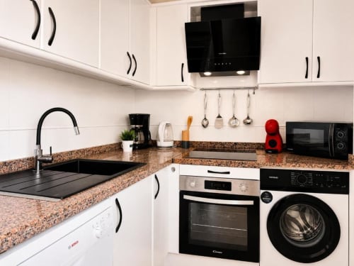 Cocina moderna en el Apartamento Duplex II de Aloha Calpe con muebles blancos, encimera de granito y electrodomésticos negros