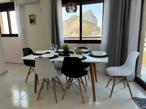 Comedor moderno en apartamento de Calpe con vistas a la montaña, mesa puesta y sillas en blanco y negro
