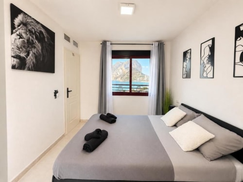 Habitación en Aloha Calpe con vistas al mar y montañas, cama negra moderna, almohadas blancas y acceso a balcón