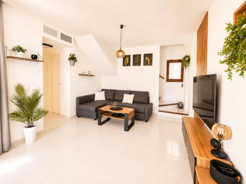 Sala de estar moderna en apartamento Duplex II de Aloha Calpe con sofá oscuro, mesa de madera, TV y plantas exuberantes