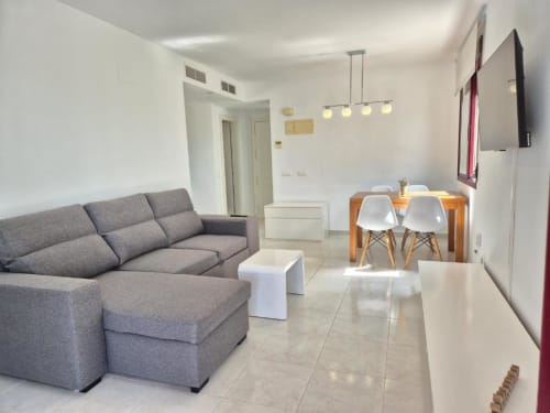 Luminoso salón moderno en el Apartamento Salinas de Aloha Calpe con sofá gris, comedor, televisor y vistas al mar