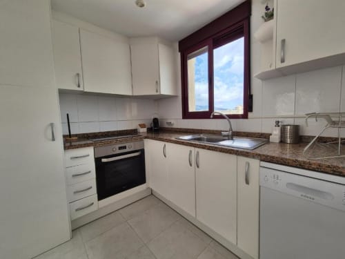 Cocina moderna en Apartamento Salinas de Aloha Calpe con gabinetes blancos, encimeras de granito y vistas al mar a través de marco burdeos