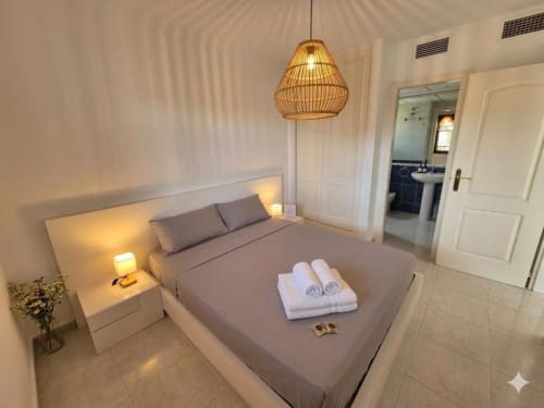 Dormitorio moderno en Apartamento Salinas de Aloha Calpe con vistas al mar, lámpara colgante de mimbre y baño en suite