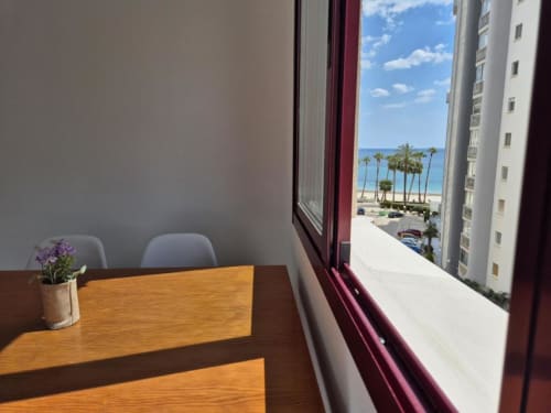Apartamento Salinas en Aloha Calpe con vistas al mar por la ventana, escritorio de madera, sillas y palmeras en la playa