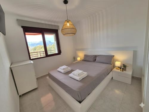 Luminoso dormitorio moderno en Apartamento Salinas, Aloha Calpe con vistas al mar y montaña, cama blanca, lámpara colgante y terraza