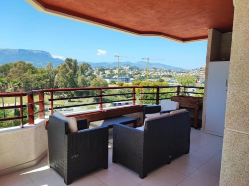Terraza con zona de descanso, toldo rojo y vistas a las montañas de Calpe y el Mediterráneo en el apartamento Aloha Calpe.
