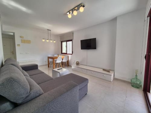 Moderna sala de estar en el Apartamento Salinas del hotel Aloha Calpe en Calpe con sofá gris, TV, comedor y cocina