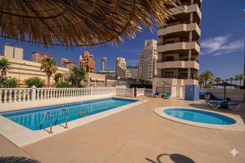 Terraza de piscinas del apartamento Aloha Calpe con dos piscinas azules, palmeras, edificios frente al mar y costa mediterránea